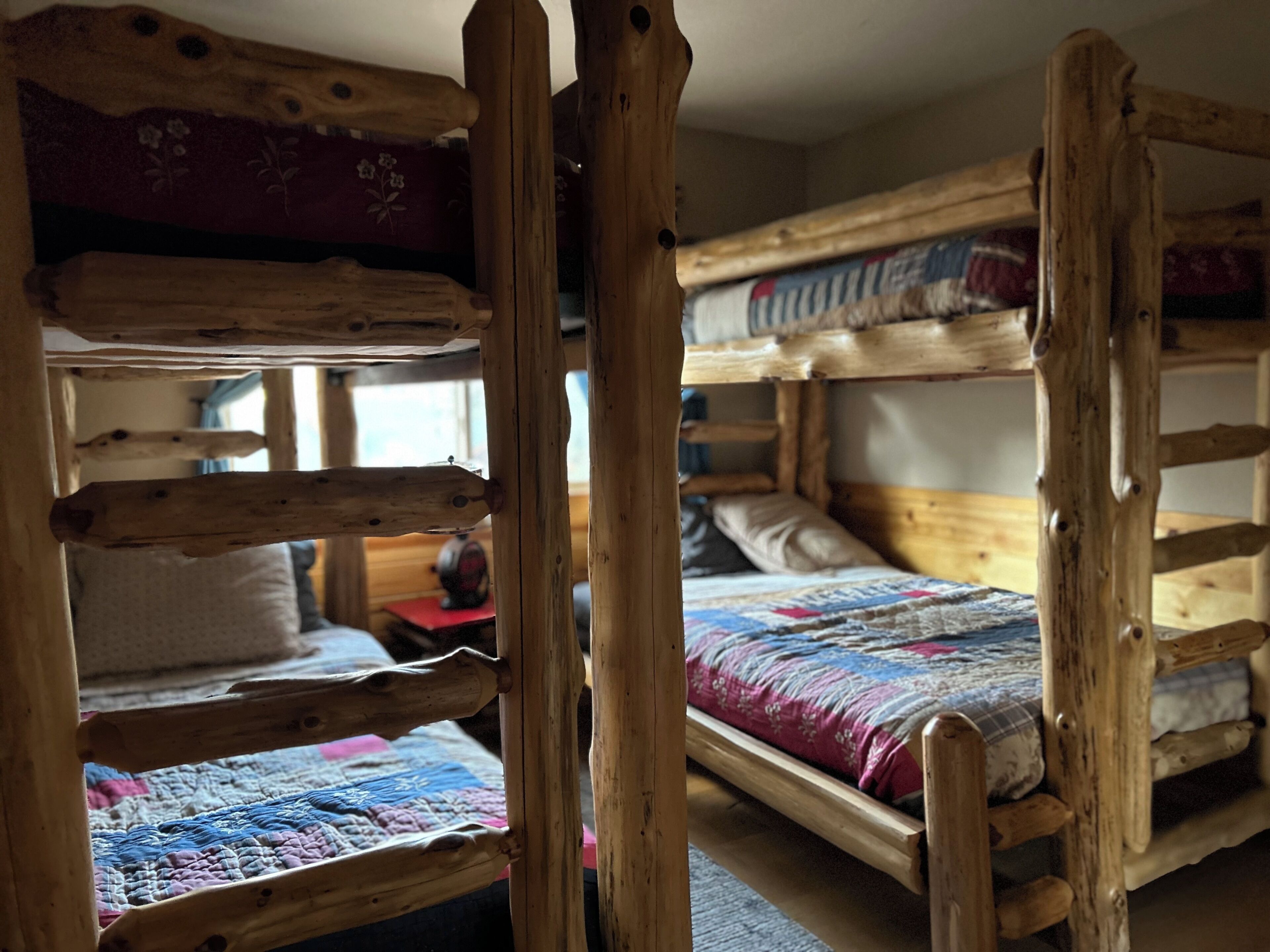 A bunk bed room with wooden railings, a quilted bedspread, and a window in the background.