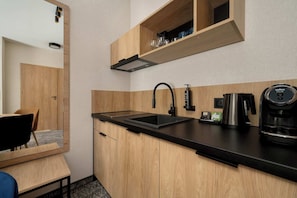 Eine kompakte Küche mit schwarzer Arbeitsplatte, Holzschränken, einer eingebauten Spüle und einer Kaffeemaschine.