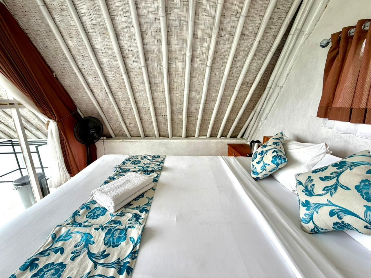 Een kamer met twee bedden, een ventilator en een raam met gordijnen.