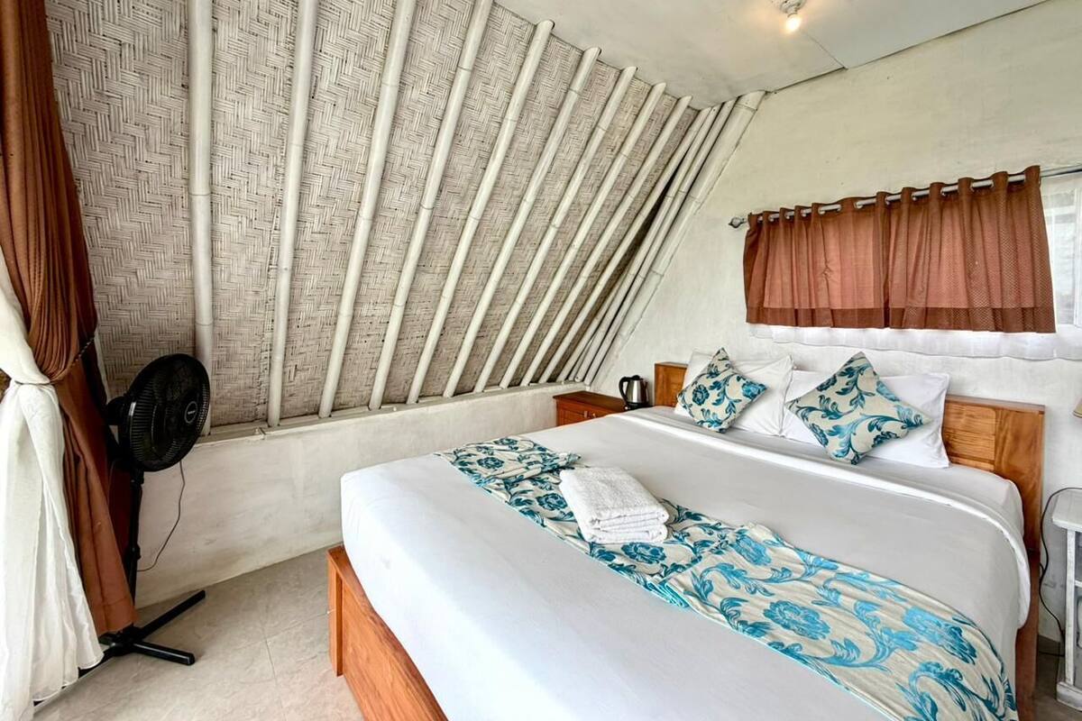 Un dormitorio con cama, ventilador, ventana con cortinas y pared con textura tejida.