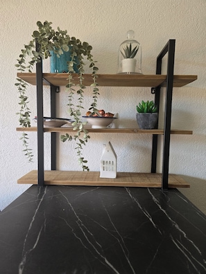 A black marble table with a wooden shelf unit holding plants, a bowl, and a small white house-shaped object.