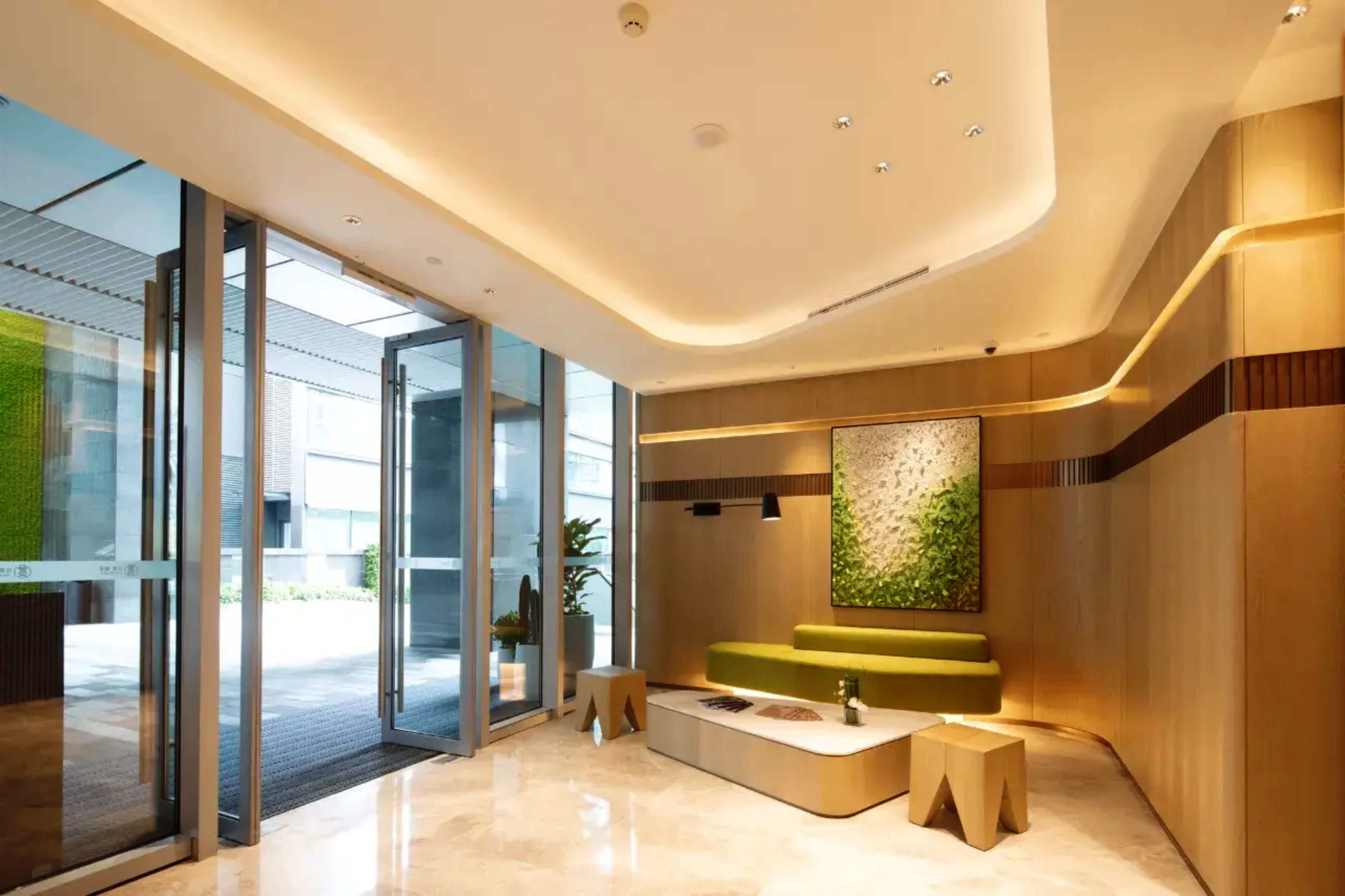 Una hall moderna con una reception, un divano verde e una parete con una pianta.