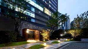 A modern building with a well-lit entrance, paved pathways, and surrounding greenery. - Hengjing Yushi Hotel (Chengdu)
