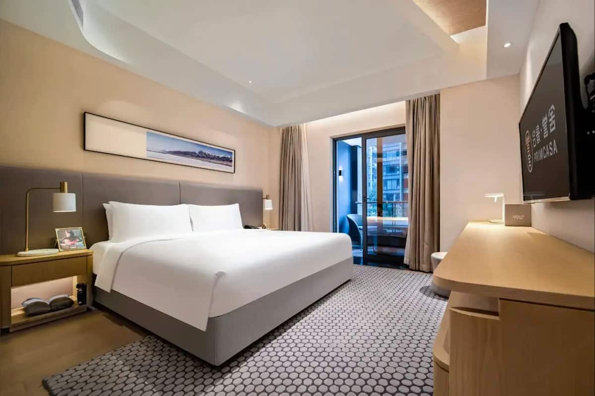 Une chambre d’hôtel avec un grand lit, un bureau, une télévision et une vue sur la ville par la fenêtre.