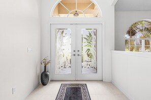 A white door with frosted glass panels, a black vase with flowers, and a patterned rug on a tiled floor. - Villa Twin Palms 3BR 2BA Waterfront Heated Pool Gulf Access Private Dock (Cape Coral)