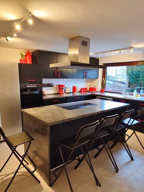 Une cuisine moderne dotée d’un îlot central, de meubles de couleur noire et d’une hotte de cuisson en acier inoxydable.