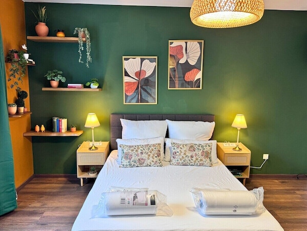 Ein Schlafzimmer mit einem Bett, zwei Nachttischen, einer Pendelleuchte und Wandbildern.