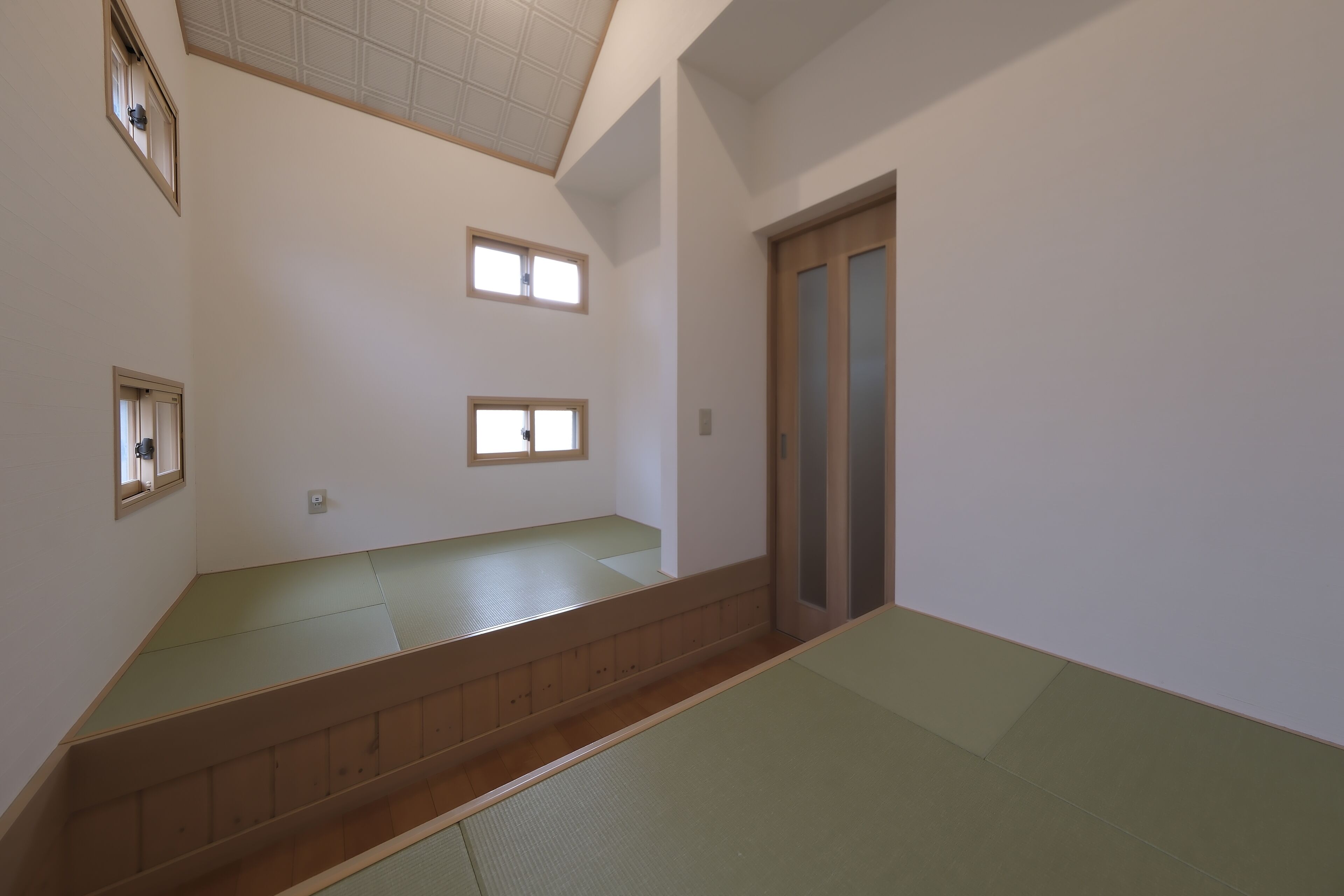 Een kamer met tatami matten, een houten bank, een schuifdeur en twee kleine ramen.