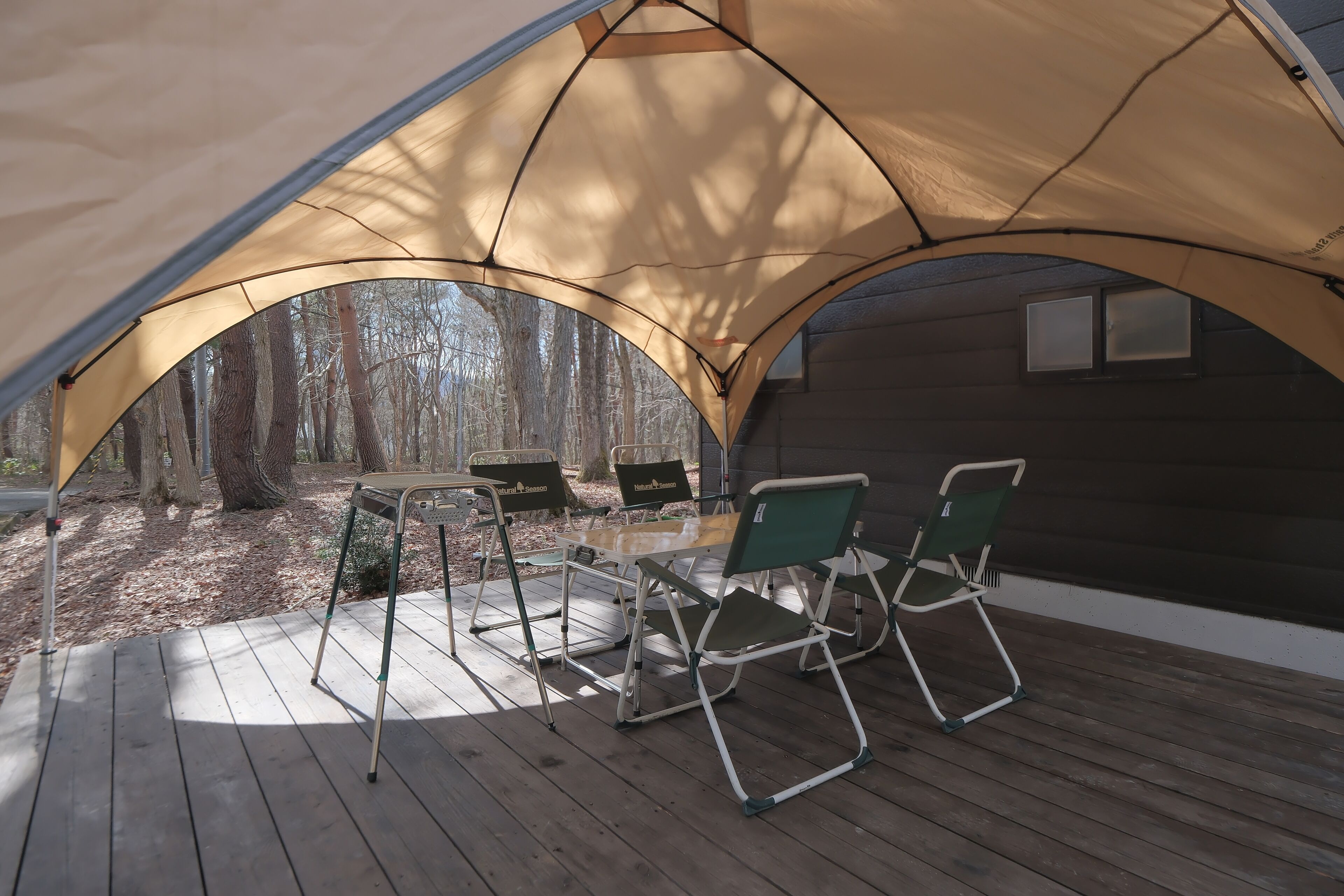 A tented outdoor area with a table and chairs, surrounded by trees.