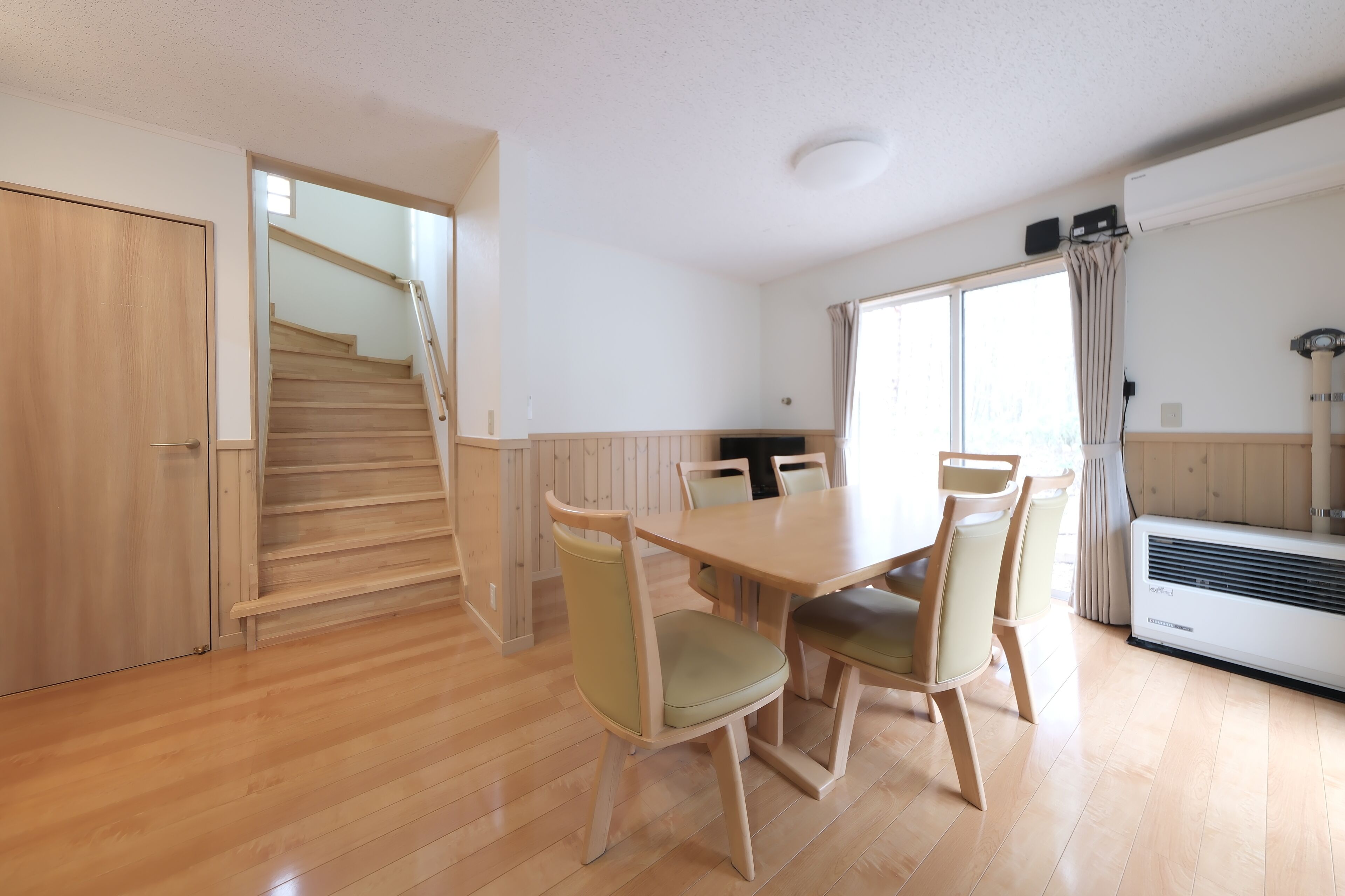 A dining area with a wooden table and chairs, a staircase, and an air conditioning unit.