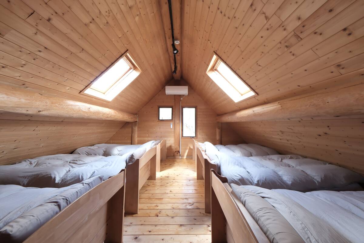 A wooden room with two beds, a skylight, and a central window.