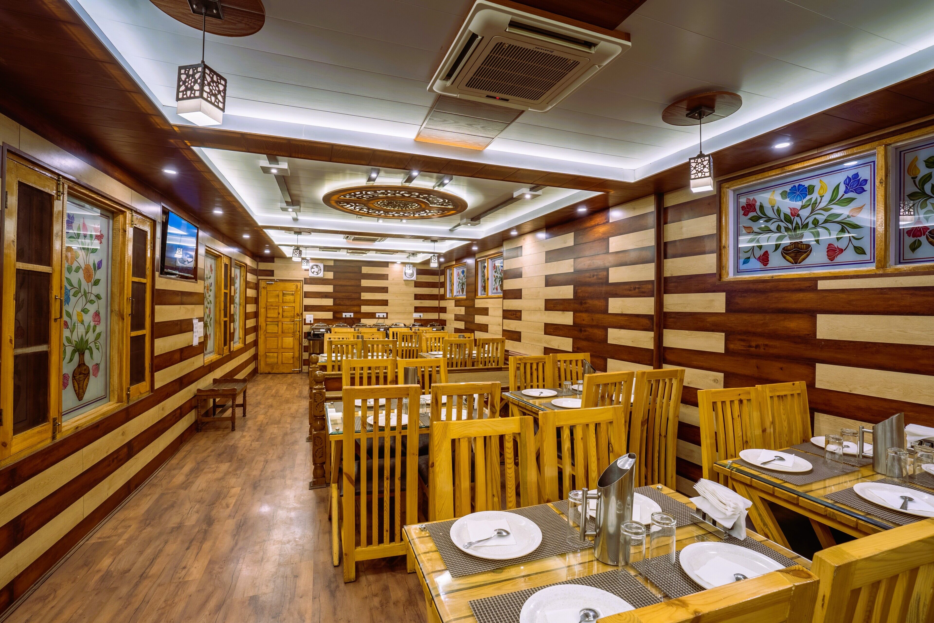 A restaurant with wooden panel walls, wooden tables with white plates, and a central aisle.