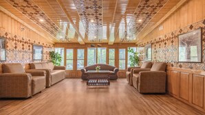 A spacious room with wooden walls and ceiling, large windows, and a central sofa. - Bombay Palace (Pahalgam)
