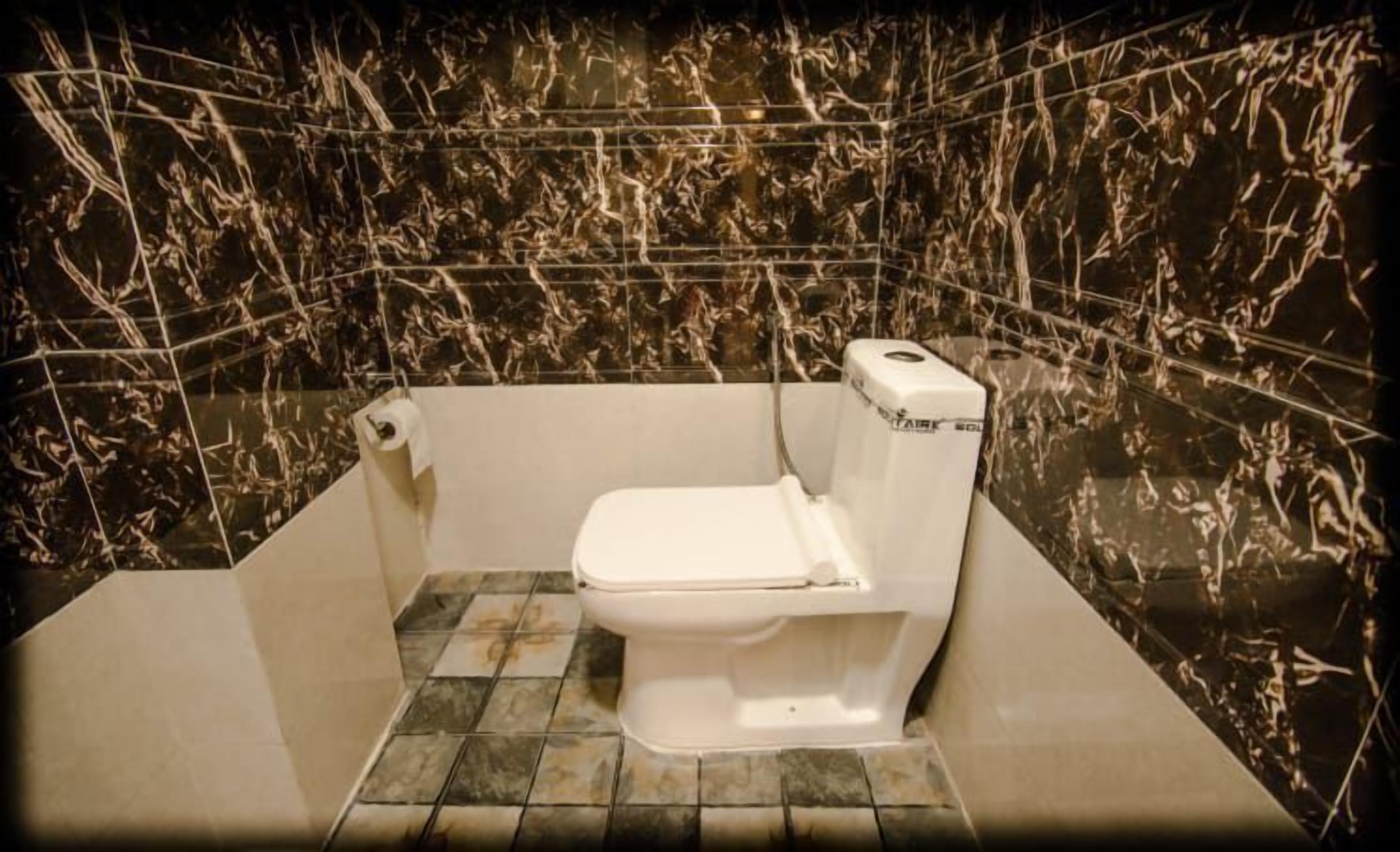 Un baño con inodoro blanco, paredes de mármol y suelo de baldosas.