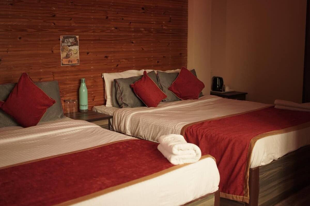 A hotel room with two beds, wooden headboard, red and white bedding, a green water bottle, and a poster on the wall.