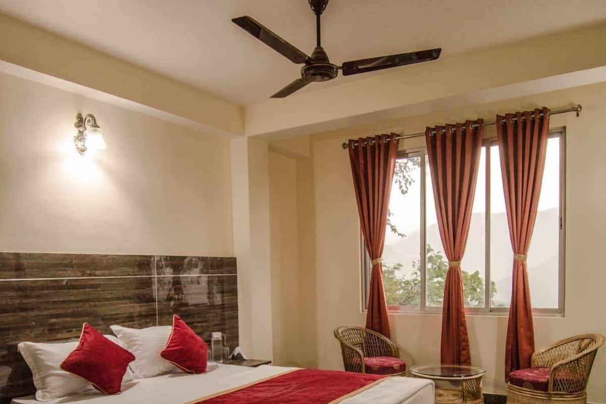 A bedroom with a bed, two chairs, a small table, a ceiling fan, and a window with curtains.