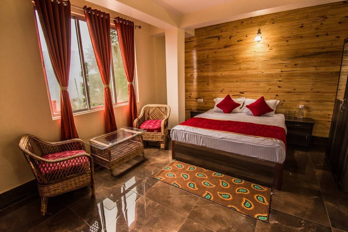 A bedroom with a wooden headboard, a bed with red pillows, two wicker chairs, a glass coffee table, and a patterned rug.