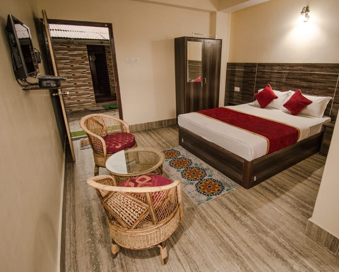Quarto de hotel com cama, guarda-roupa, televisão, espelho, mobiliário de vime e tapete estampado.
