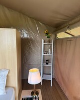 Quarto com tenda, cama branca, luminária, prateleira com vaso e lanternas, e um menu no chão.