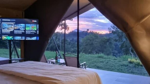 A bedroom with a bed, a TV on a stand, and a view of the outdoors. - Tikumbar - Glamping, Cafe, Camping Ground & Campervan (Pelaga)