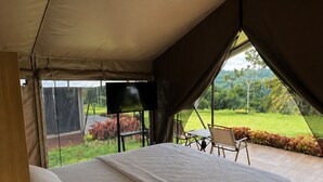 A tented room with a bed, a TV, and a view of a garden. - Tikumbar - Glamping, Cafe, Camping Ground & Campervan (Pelaga)
