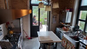 Een keuken met een fornuis, wastafel en een tafel. Er is een raam met uitzicht op groen.
