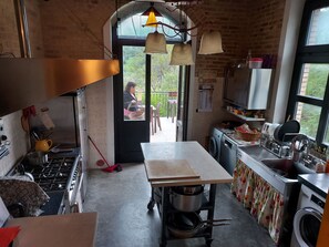 A kitchen with a stove, sink, and a table. There is a window with a view of greenery outside.