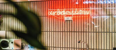 A kitchen with a microwave, sink, and a neon sign on the wall.