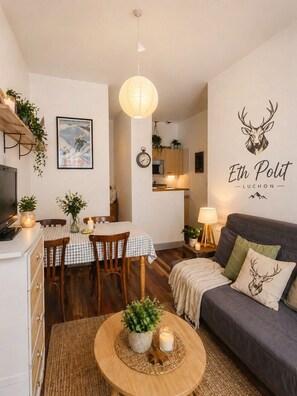 Ein gemütliches Wohnzimmer mit einer Couch, einem Esstisch mit Stühlen, einem Fernseher und einer Wand mit einem Logo.