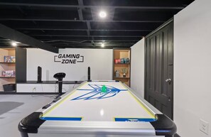 A pool table in a room labeled 'GAMING ZONE' with a ceiling fan, shelves with board games, and a door. - The Elevated Pine Escape | Hot Tub + Game Room (Albrightsville)