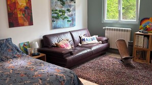 Makuuhuoneessa on sänky, nahkasohva, patteri, ikkuna ja taideteoksia seinillä.