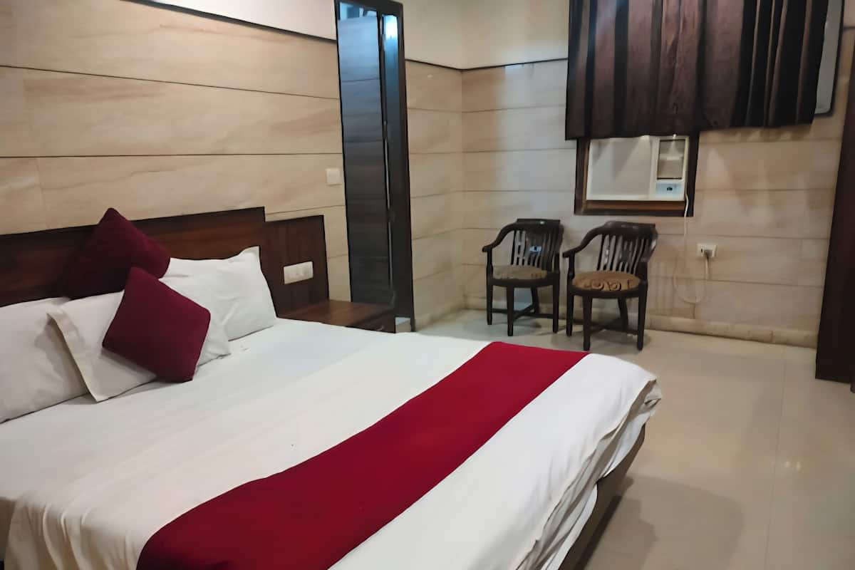 A hotel room with a large bed, a red and white bedspread, two wooden nightstands, a mirror, two wooden chairs, and a wall-mounted air conditioning unit.