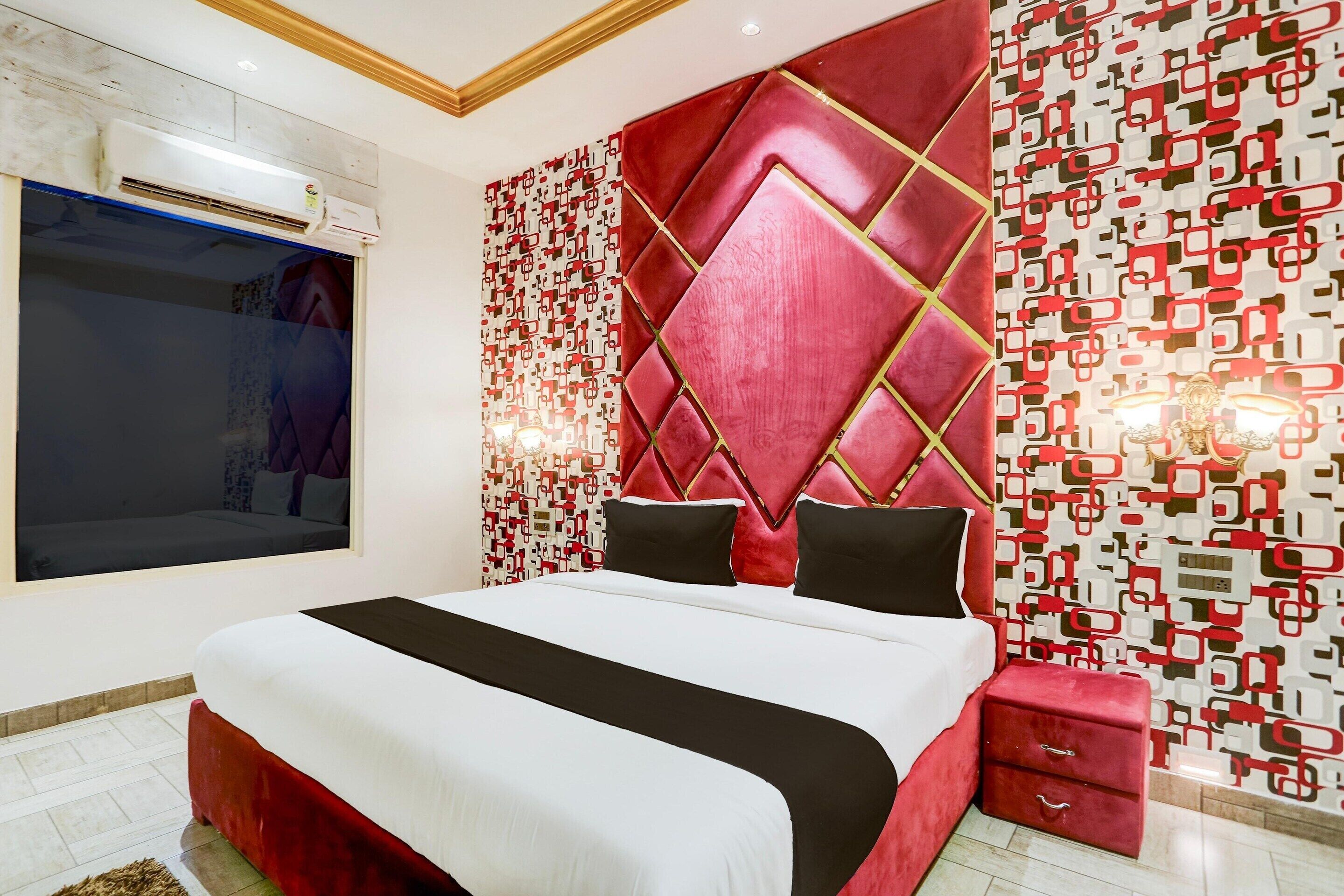 Un dormitorio moderno con una cama grande, cabecera roja, papel tapiz estampado y mesita de noche roja.
