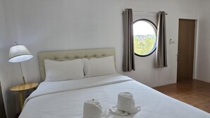 A hotel room with a bed, a round window, curtains, a lamp, and towels on the bed. - FIELD GOOD Resort at Chiang Rai (Chiang Rai)
