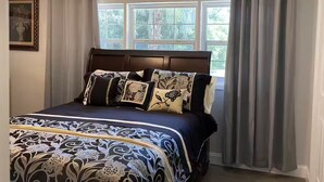 A bedroom with a bed, a ceiling fan, a window with curtains, and a framed picture on the wall.