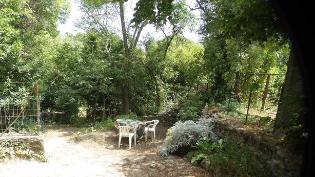 A garden with a table and chairs, surrounded by trees and a stone wall. - Small pied-à-terre in the countryside (Causse-de-la-Selle)
