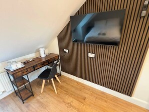 Una habitación moderna con un panel de madera listonada, un televisor de pantalla plana sobre un escritorio, una silla y un radiador.