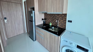 A modern kitchen with wooden cabinets, a stainless steel refrigerator, a black countertop, a sink, and a built-in washing machine. - Nam Talay by PSR (Nongprue)