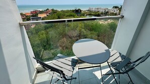 A balcony with a table and chairs, overlooking a coastal area with buildings and greenery. - Nam Talay by PSR (Nongprue)