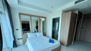A modern hotel room with a large bed, a wardrobe, a television, and a bathroom visible through a glass door. - Nam Talay by PSR (Nongprue)