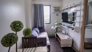 En kompakt opholdsstue med sofa, spisebord, tv og en lille plante.