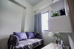 Ein Zimmer mit einer Couch, einem kleinen Tisch, einer Topfpflanze und einem Fenster mit Vorhängen.