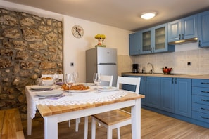 Eine Küche mit blauen Schränken, einer Steinsäule, einem weißen Tisch mit Spitze und einem Kühlschrank.