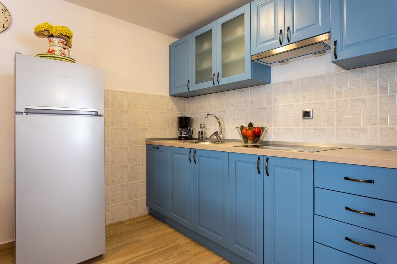 A kitchen with blue cabinets, a white refrigerator, a sink, and a vase with flowers on the counter.