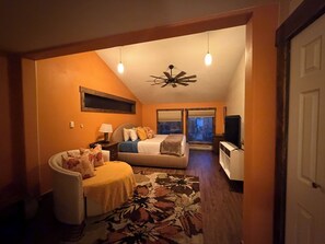 Une chambre confortable avec un lit, un bureau et une chaise. On y trouve un ventilateur de plafond et une fenêtre avec des stores.