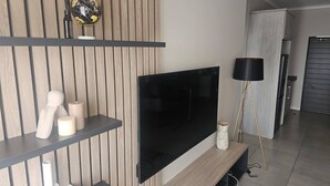 Un salon moderne doté d’un téléviseur à écran plat, d’un mur recouvert de panneaux en bois, d’étagères ornées d’objets décoratifs et d’un lampadaire.