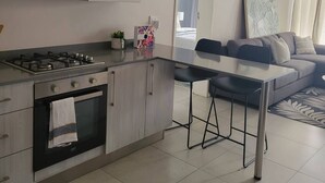 Une cuisine moderne équipée d’une cuisinière à gaz, d’un four et d’une hotte en acier inoxydable. On y trouve un coin repas avec une table et des chaises, ainsi qu’un canapé dans le salon.