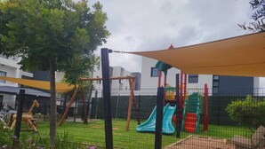 Un espace de jeux extérieur clôturé, équipé d’un toboggan, de structures d’escalade et d’un coin salon ombragé.