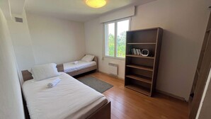 A room with two single beds, a bookshelf, a radiator, and a window with a view of greenery. - Villa du Cedre | House & Garden, Montrabe (Montrabé)
