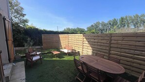 A backyard with a wooden fence, a round table with chairs, and a small garden area. - Villa du Cedre | House & Garden, Montrabe (Montrabé)